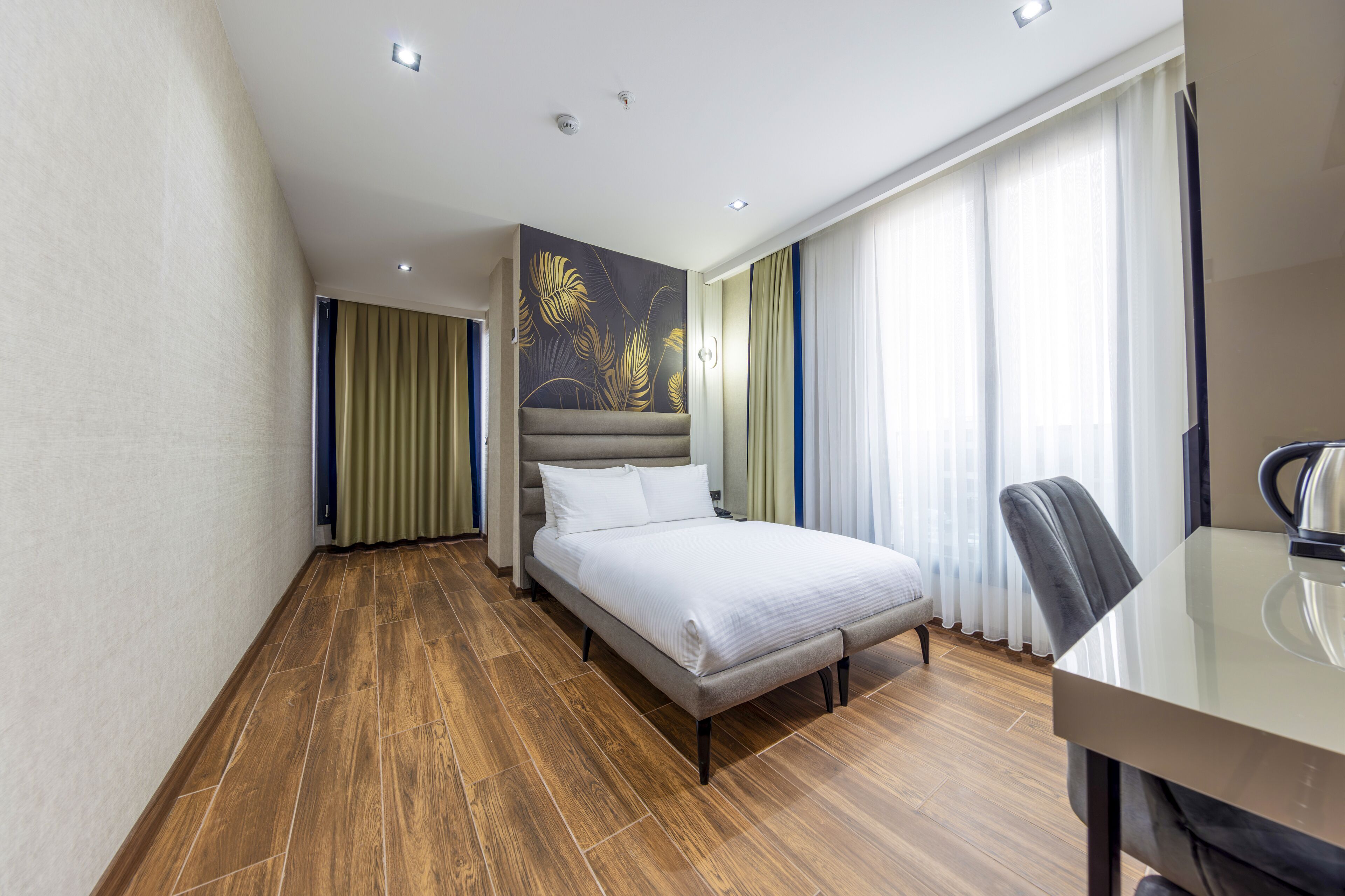 A modern hotel room with a large bed, a desk, and a view of the city through the window.