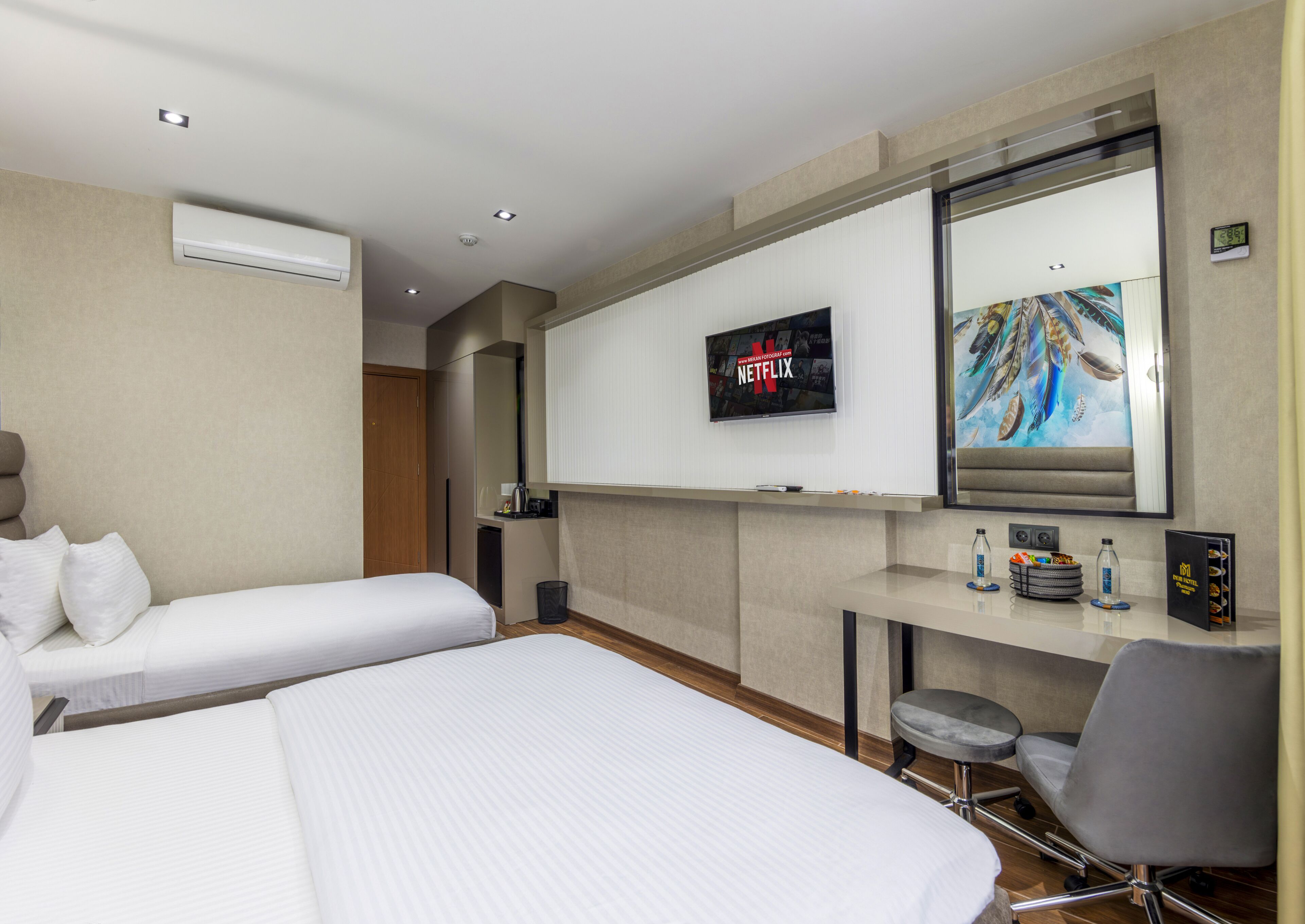 A hotel room with two beds, a desk with a chair, a TV, and a painting on the wall.