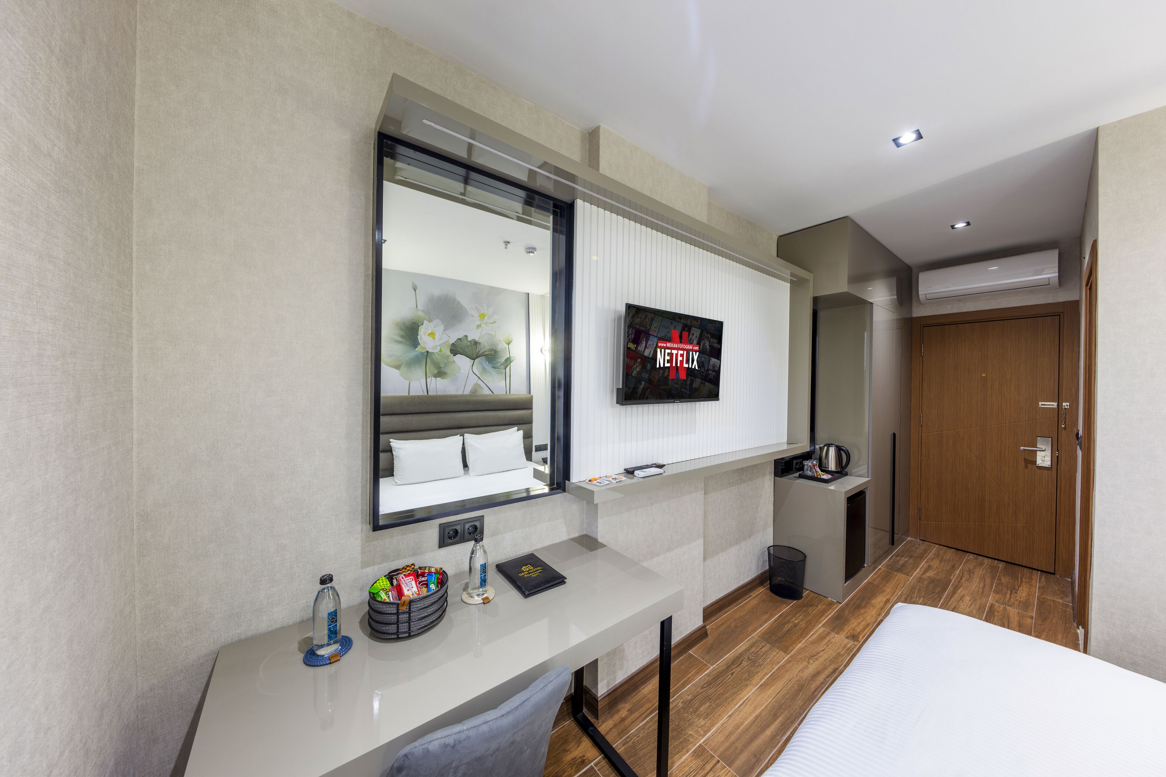 A modern hotel room with a large bed, a desk with a flat-screen TV, a mirror, and a wooden wardrobe.