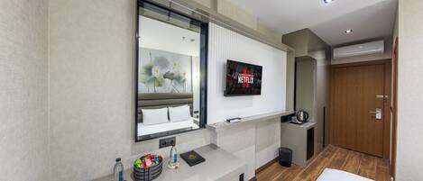 Une chambre d’hôtel moderne dotée d’un grand lit, d’un bureau avec un téléviseur à écran plat, d’un miroir et d’une armoire en bois.