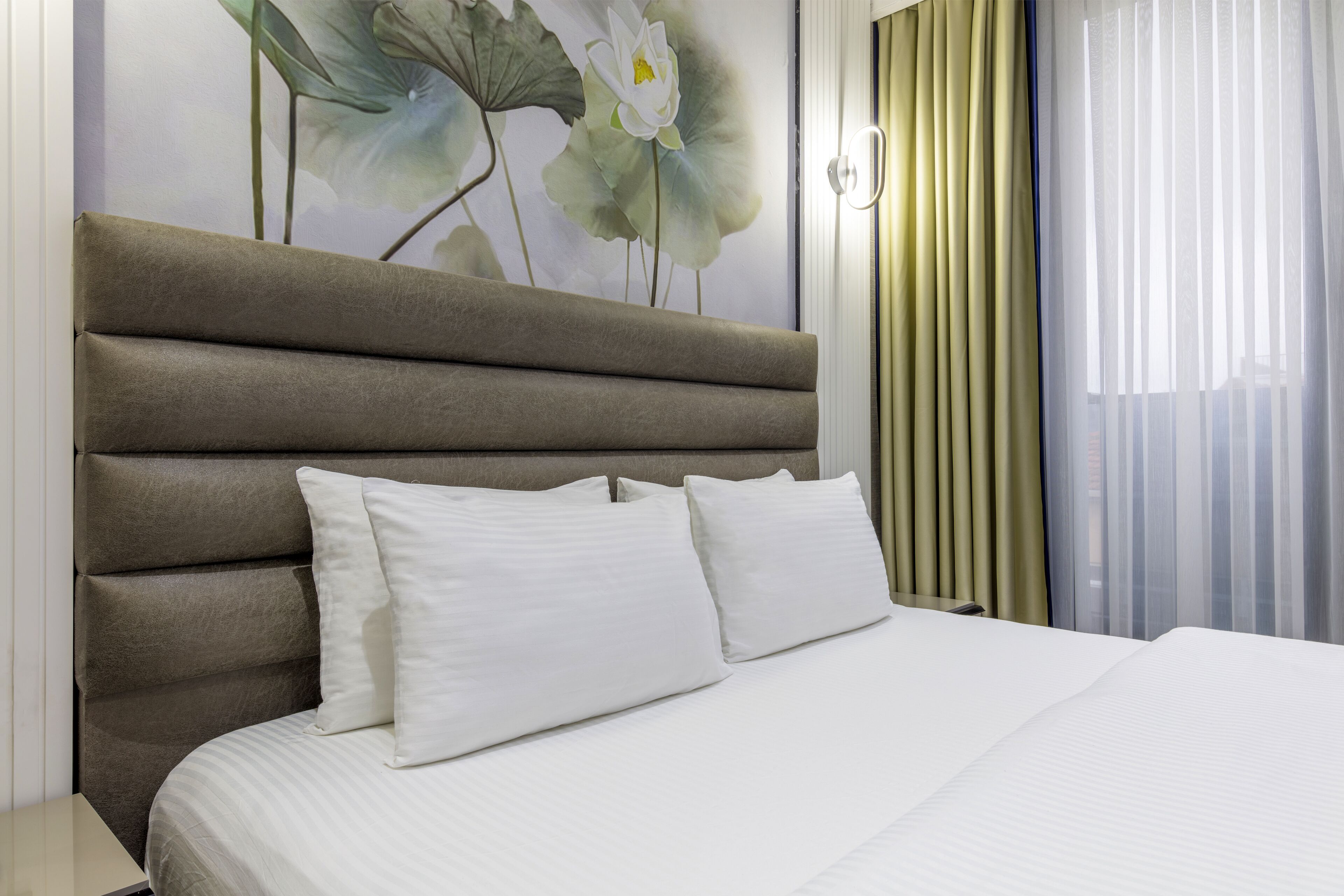 Una habitación de hotel con una cama grande, un cabecero y un cuadro de flores en la pared.