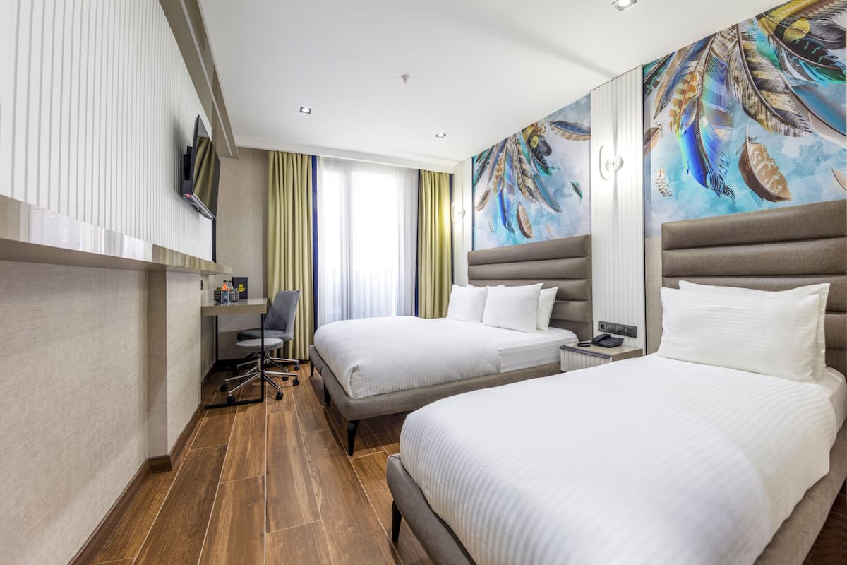 A hotel room with two beds, a desk, a chair, and a painting on the wall.