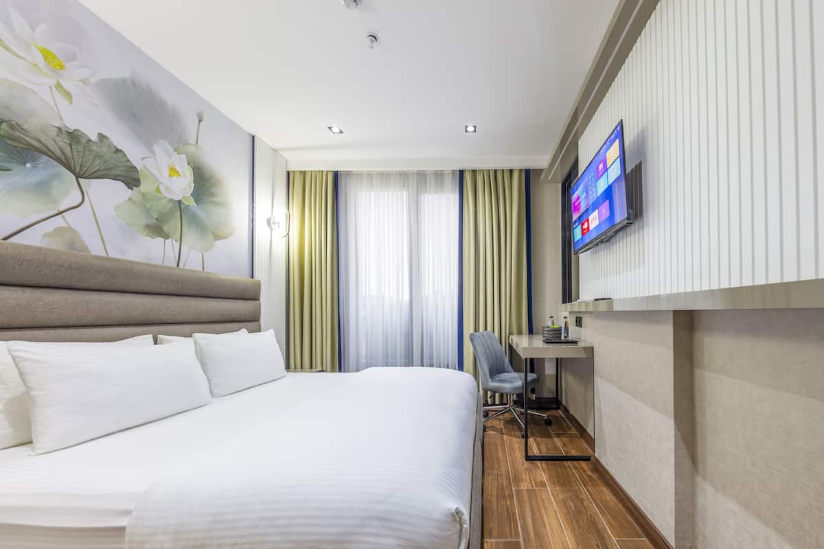 A hotel room with a large bed, a desk, a chair, a television, and a wall-mounted TV.