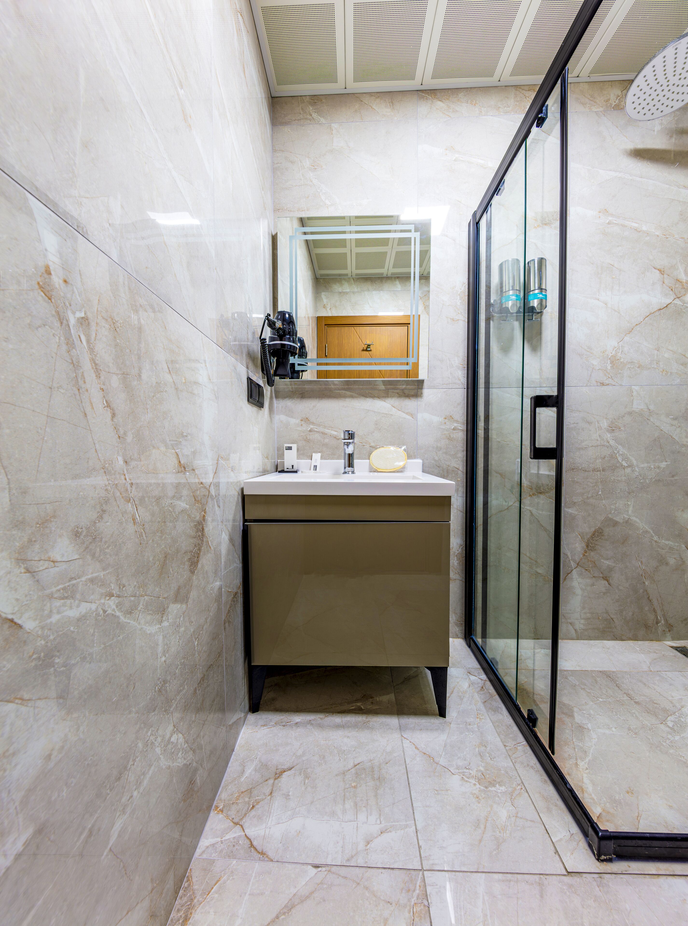 Un baño con piso de mármol, cabina de ducha de vidrio y tocador con espejo.
