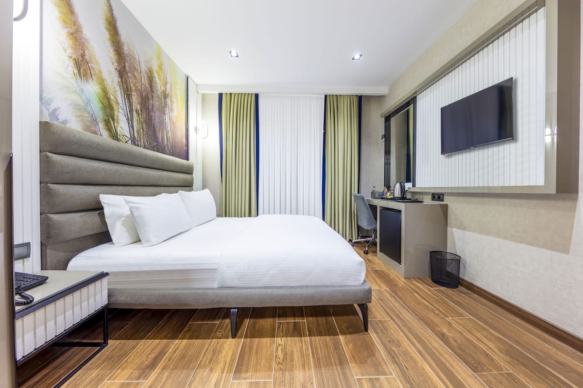 A modern hotel room with a large bed, a desk, a television, and a painting on the wall.