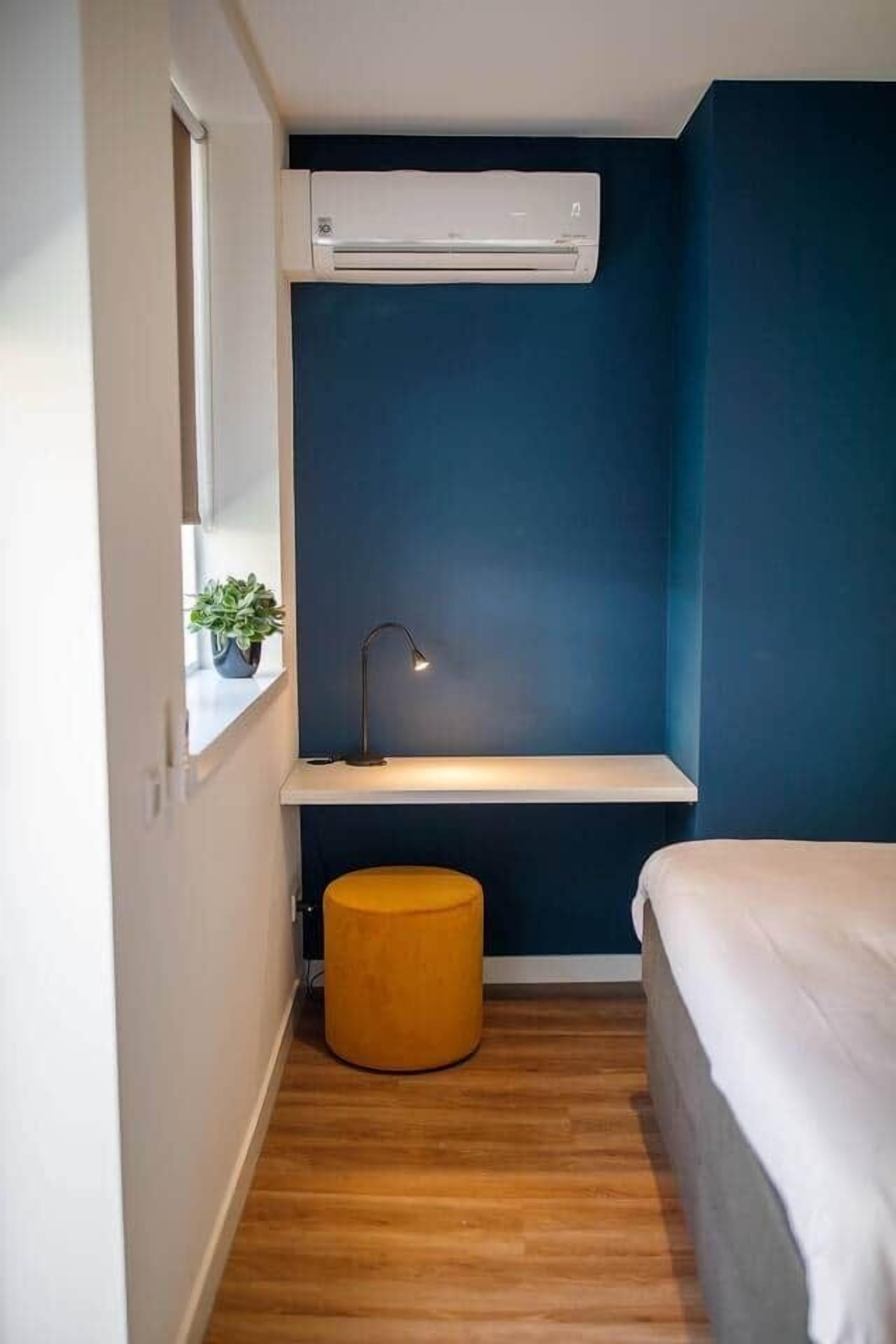 Ein kleines Schlafzimmer mit einem Bett, einem Nachttisch, einer Lampe und einer an der Wand befestigten Klimaanlage.