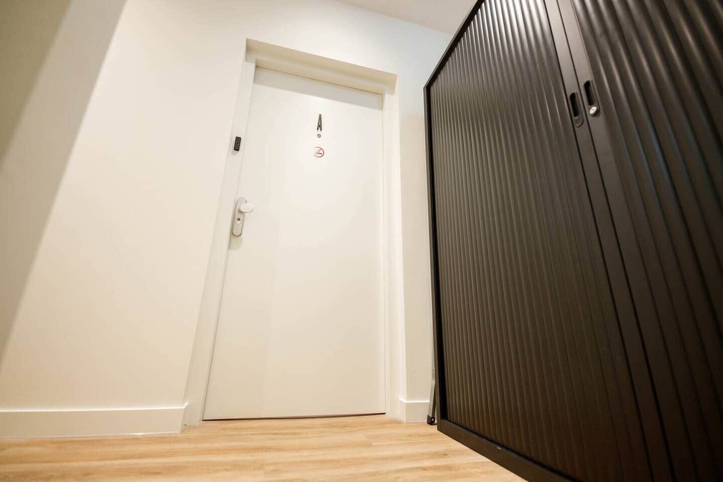 En gang med en hvid dør, trægulv og en stor sort garderobe.