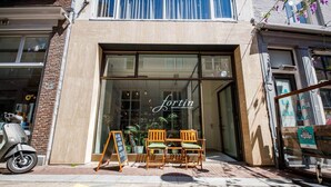 A storefront with a large glass window and a sign that reads "Fortin specialty coffee & gear." There are two wooden chairs outside the entrance, and a scooter parked to the left.