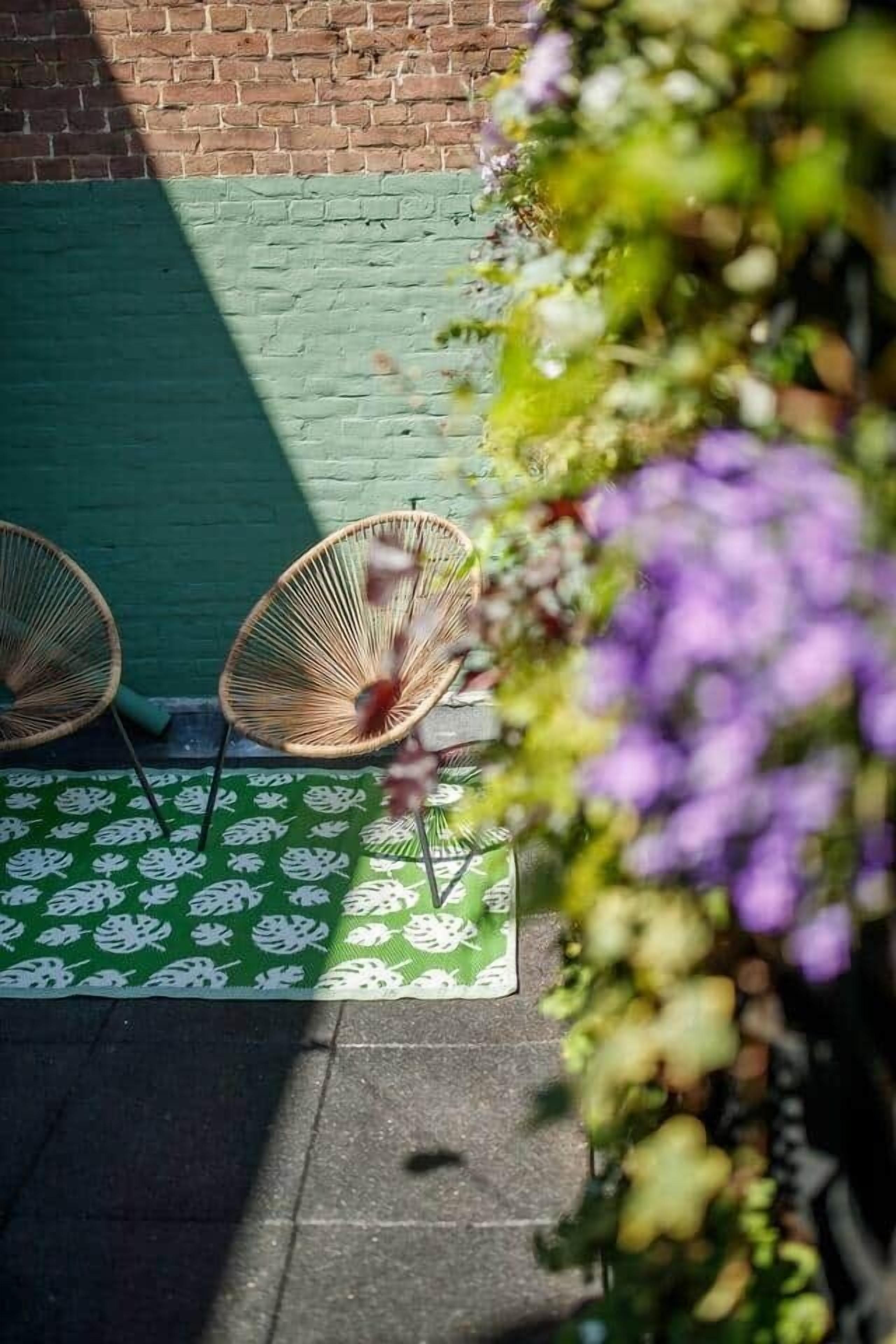 Un espace patio avec deux fauteuils en osier, un tapis à motifs verts et un mur en briques.