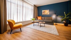 A modern living room with a sofa, armchair, coffee table, and a large window with curtains.