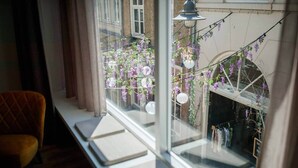 A room with a large window overlooking a balcony with purple flowers and hanging decorations.