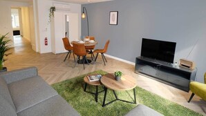 A modern living room with a dining area, a flat-screen TV, and a sofa.