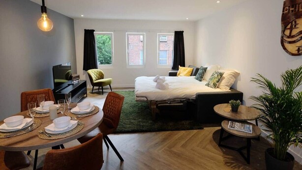 A modern hotel room with a bed, a desk, a dining area, and a large window.