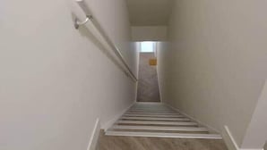 A narrow, carpeted stairway with white walls and a metal handrail.