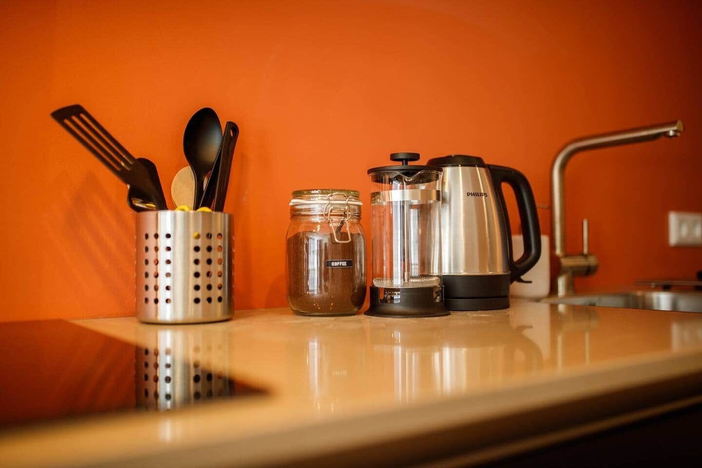 Un comptoir de cuisine avec une machine à café, un bocal étiqueté « CAFÉ » et des ustensiles rangés dans un porte-ustensiles.
