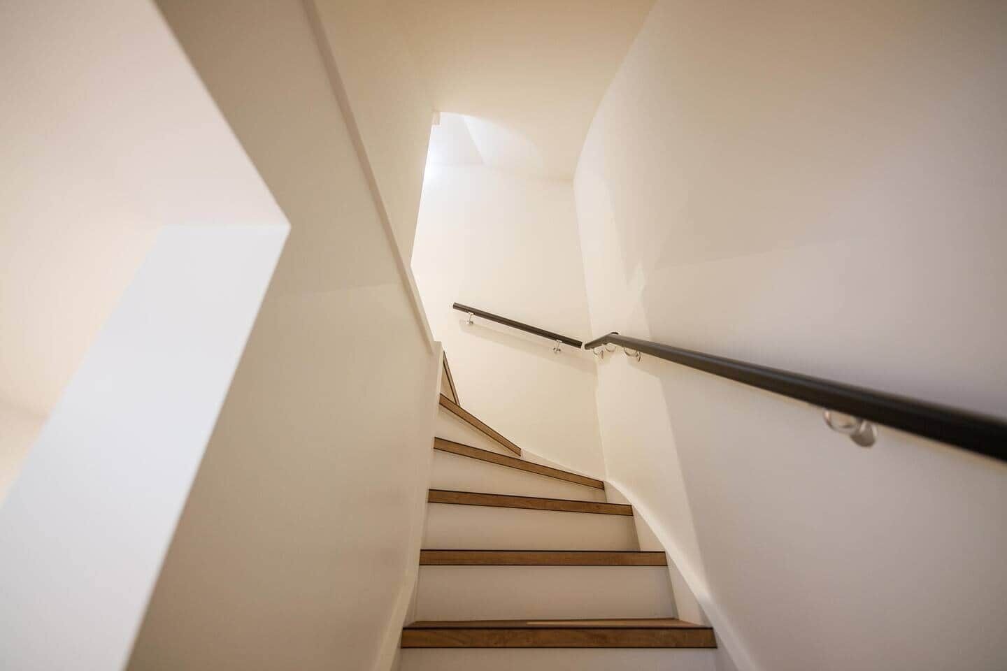 A staircase with wooden steps and a metal handrail, leading upwards in a modern interior space.