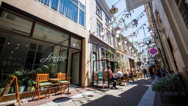 Una calle con mesas al aire libre, una cafetería llamada 'Fortin' y un cartel que dice 'SAN & M'.