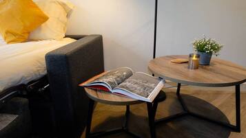 A modern hotel room with a bed, a reading chair, a small round table with a candle, and a potted plant.