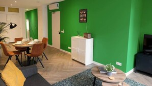 A modern living room with a green accent wall, a dining area with a round table and chairs, a sofa, and a TV. - Luxury 60m2 Apartment with Terrace (R-65-A) (Eindhoven)
