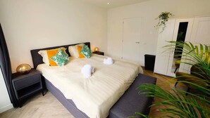 A modern bedroom with a large bed, bedside tables, a bench, a wardrobe, and a potted plant. - Luxury 60m2 Apartment with Terrace (R-65-A) (Eindhoven)