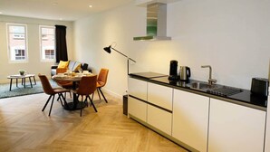 A modern kitchen with a dining area, featuring a black countertop, stainless steel sink, and a built-in range hood. - Luxury 60m2 Apartment with Terrace (R-65-A) (Eindhoven)