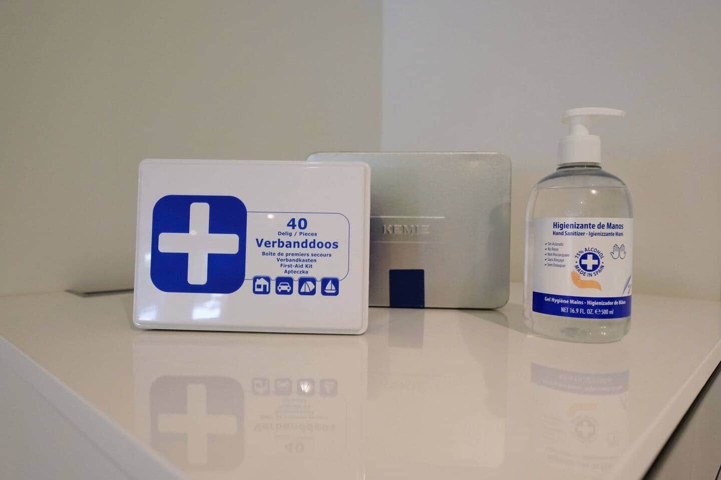 Un botiquín, una caja y una botella de gel antibacterial sobre una superficie blanca.