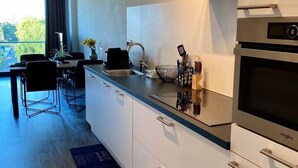 A modern kitchen with a built-in oven, a stainless steel range hood, and a dining area with a table and chairs. - Fantastic Studio with free private car parking ('s-Hertogenbosch)