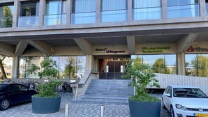 A modern building with a staircase leading to a door marked "Stella & Bergmanns." There are two potted plants in the foreground and parked cars on the pavement. - Fantastic Studio with free private car parking ('s-Hertogenbosch)