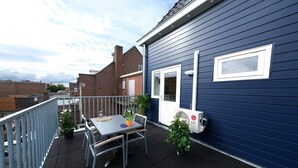 En tagterrasse med et bord, stole, en potteplante og en aircondition.