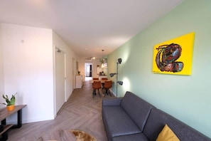 Ein modernes Wohnzimmer mit einer Couch, einem Essbereich mit Stühlen und einer Küche im Hintergrund.