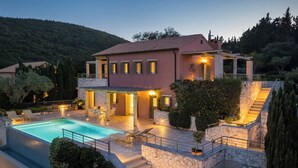 Una casa de dos pisos con piscina, mobiliario exterior y una escalera de piedra.