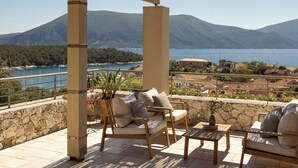 Una terraza con muebles de madera, un muro de piedra y vistas a un lago y montañas.