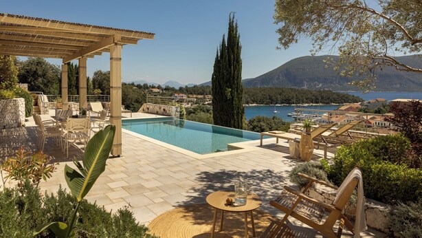 Zona de piscina con una pérgola, sillas de descanso y vistas al mar y a las montañas.