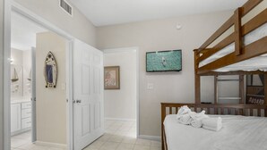 Une chambre avec un lit superposé, un téléviseur fixé au mur et une porte donnant sur une salle de bain.