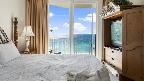 Une chambre d’hôtel avec un lit, une télévision, un balcon donnant sur l’océan et une armoire en bois.