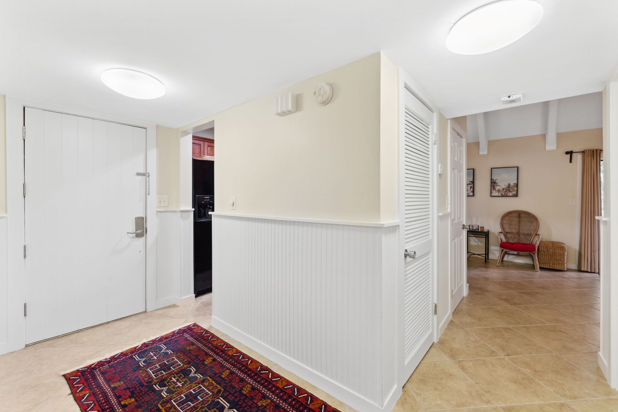 A hallway with white walls, a patterned rug, and a door leading to a kitchen.