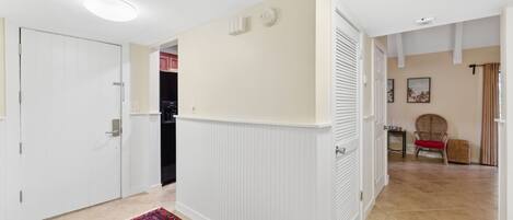 A hallway with white walls, a patterned rug, and a door leading to a kitchen.