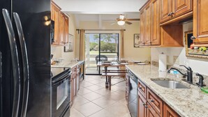 A kitchen with wooden cabinets, a black refrigerator, a granite countertop, and a view to the outside. - Seascape Villa 35D*Quiet Villa*Beach Access*Pools* (Miramar Beach)