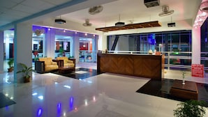 Un hall d’hôtel moderne avec un comptoir d’accueil, un espace salon et de grandes fenêtres.