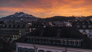 A cityscape with a prominent mountain in the background, a clock tower, and various buildings with distinct architectural styles. - Hotel Goldener Stern – Self check-in (Lucerne)