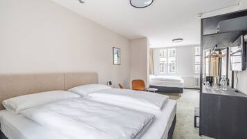 Ein Hotelzimmer mit zwei Betten, einem Schreibtisch, einem Stuhl, einem Spiegel und einem Fenster mit Blick auf Gebäude.