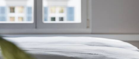 Un lit avec une literie blanche dans une pièce dotée d’une fenêtre.