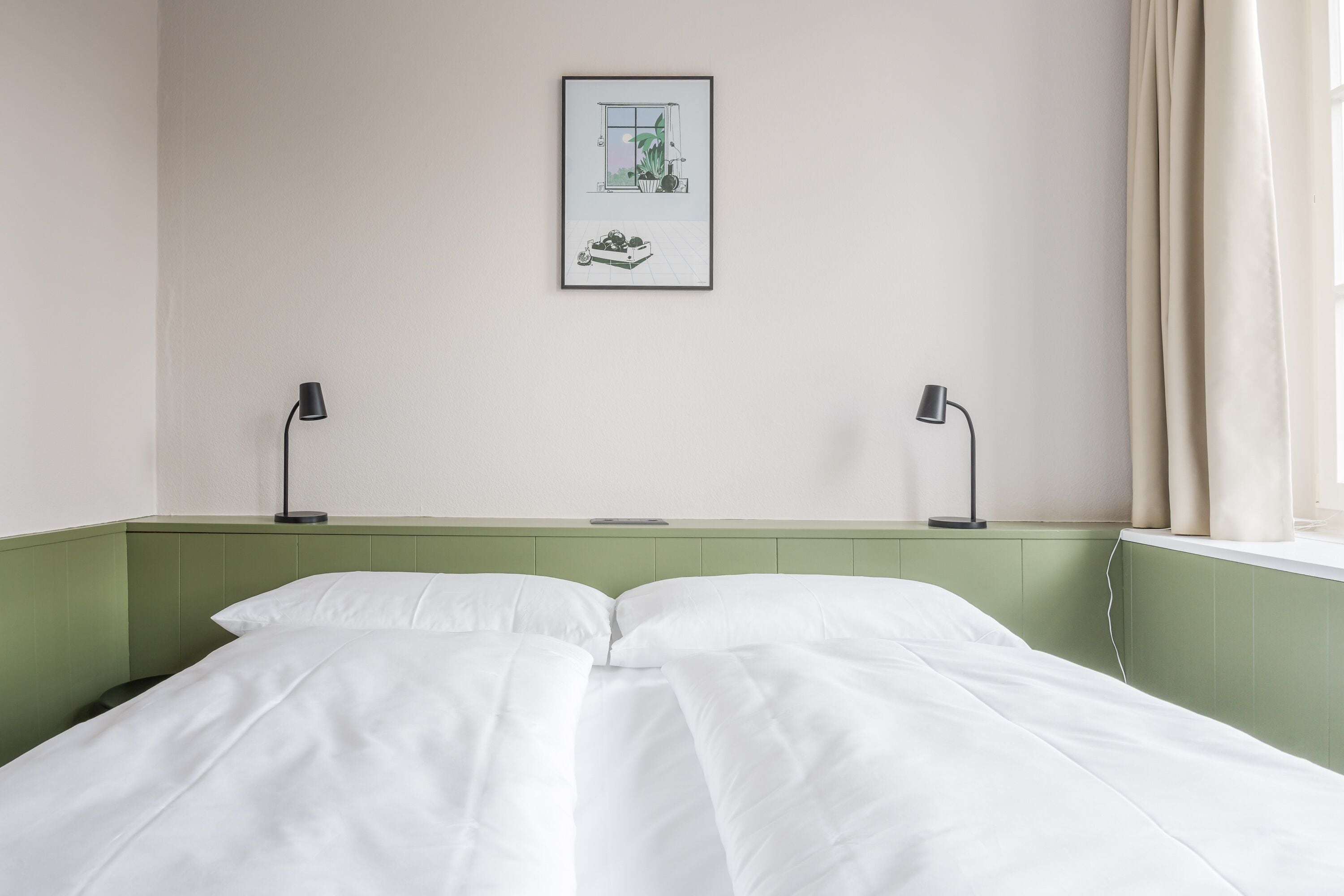 Een net opgemaakt bed met witte lakens, een ingelijst schilderij aan de muur en twee bedlampjes.