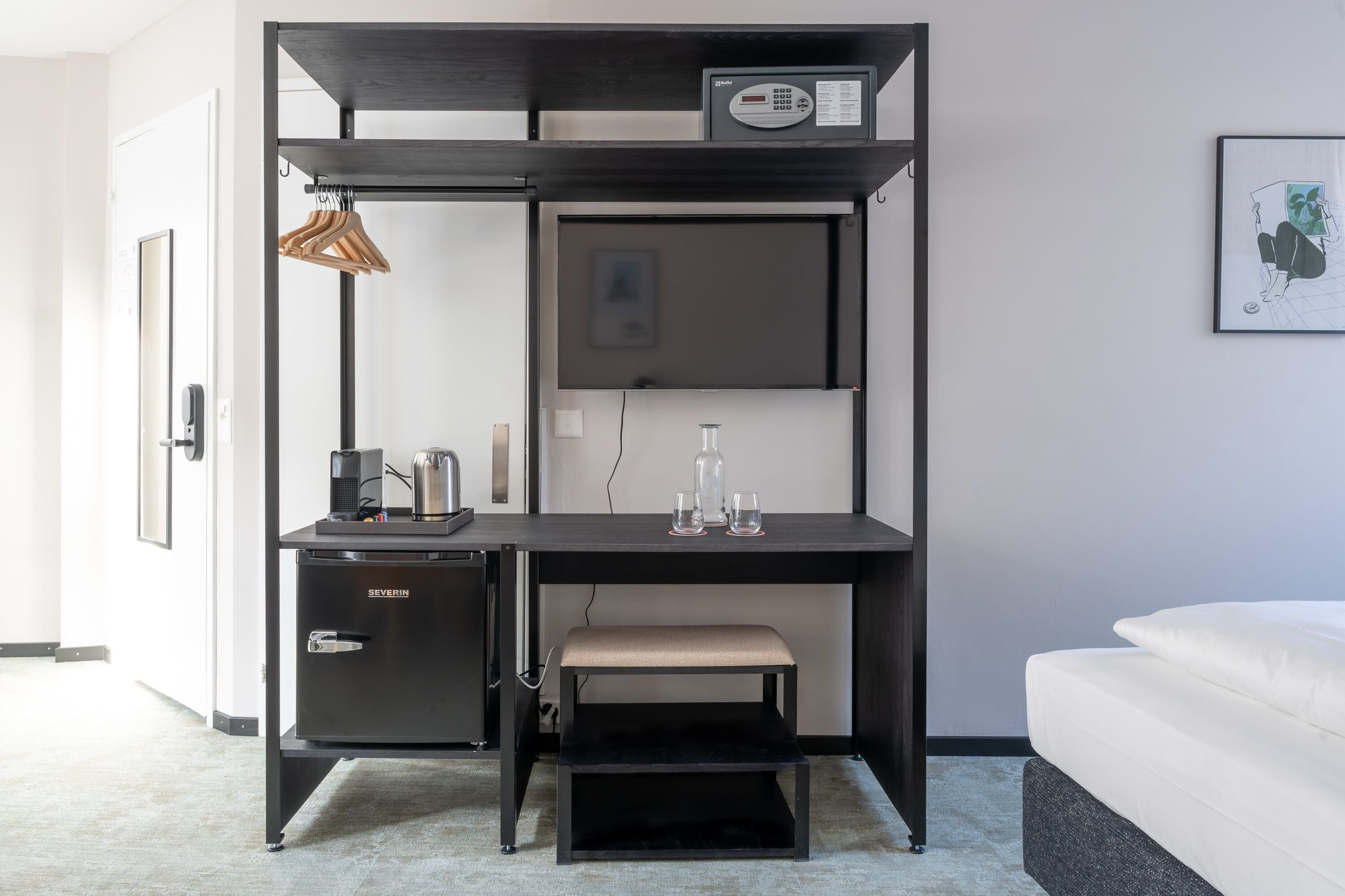 Una habitación compacta y moderna con escritorio integrado, una banca, un mueble pequeño y una cama.