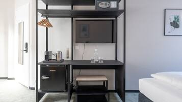 Una habitación compacta y moderna con escritorio integrado, una banca, un mueble pequeño y una cama.