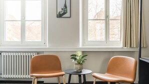 A room with two orange chairs around a small table with a potted plant, large windows with curtains, and a radiator. - Hotel Goldener Stern – Self check-in (Lucerne)