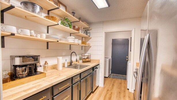 A modern kitchen with wooden shelves, a coffee maker, and a stainless steel refrigerator.