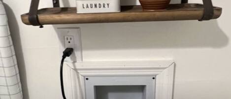 A Samsung self-cleaning smart core washing machine with a control panel, a care instructions box, and a brown vase on a shelf above.