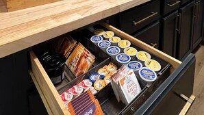 A modern kitchen with wooden shelves, a coffee maker, and a variety of packaged goods.