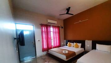 Habitación de hotel con cama, ventilador de techo, ventana con cortinas rojas y equipo de aire acondicionado.